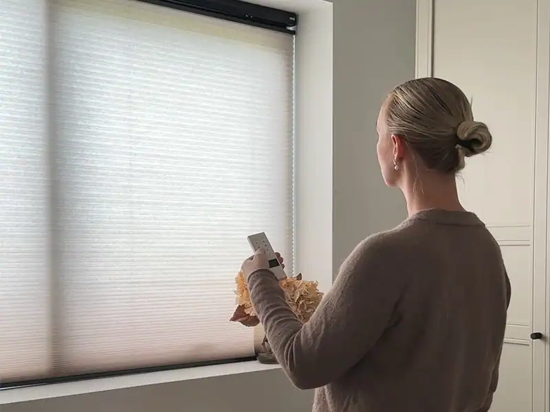 Ung kvinde betjener motoriserede up and down plisségardiner med fjernbetjening.